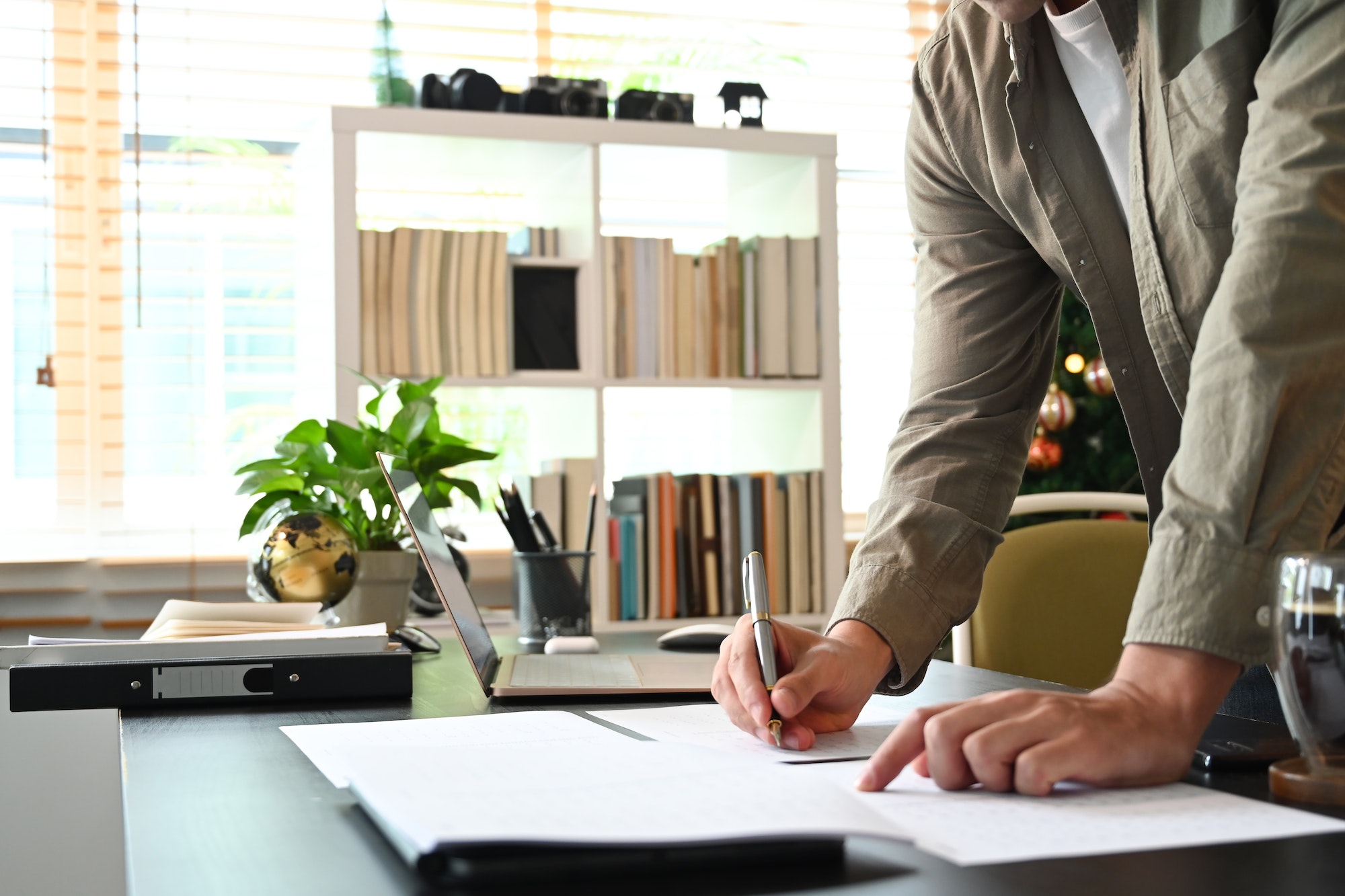 Cropped shot young man standing in home office and writing information on document.